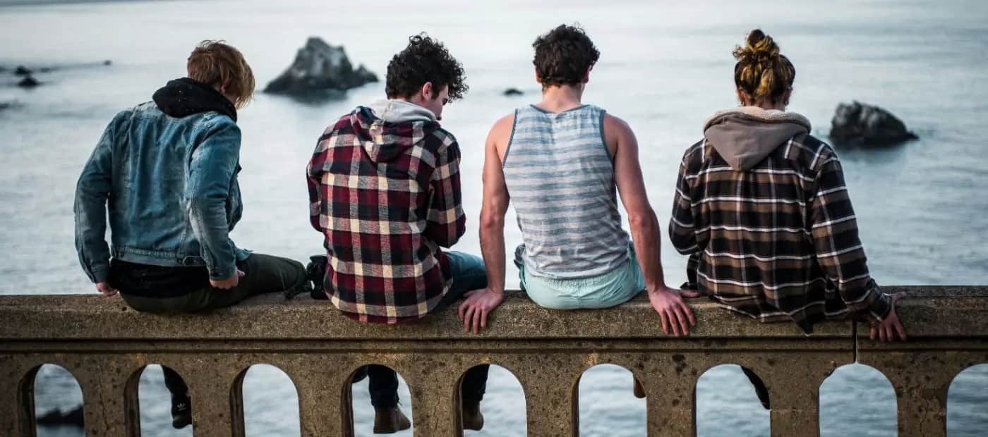 Four friends sitting side by side on a seaside wall, looking out over the water