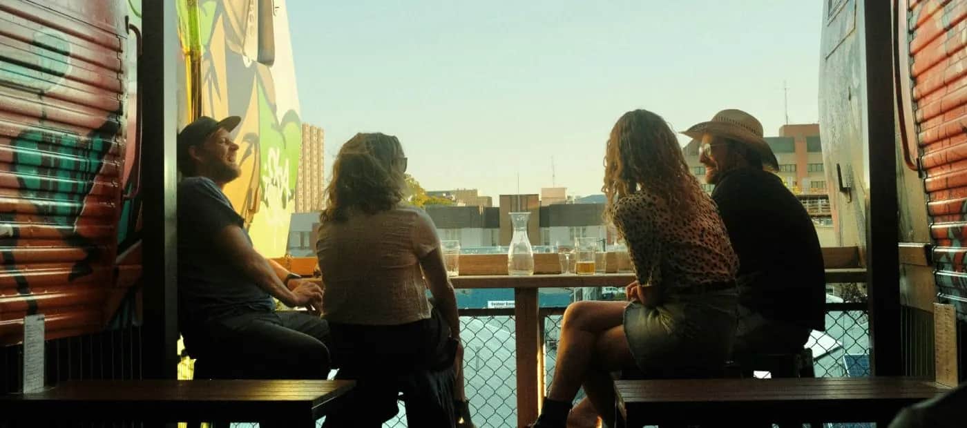 Two pairs of friends chatting at a rooftop bar table in the late-afternoon sun